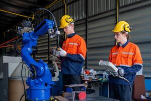group of male engineer workers maintenance automatic robotic arm machine in a dark room factory. worker checking and repairing automatic robot hand machine. Worker wearing safety glasses and helmet. photo