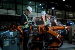 team engineers inspecting on machine with smart tablet. Worker works at heavy machine robot arm. The welding machine with a remote system in an industrial factory. Artificial intelligence concept. photo