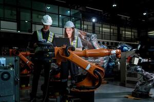 team engineers inspecting on machine with smart tablet. Worker works at heavy machine robot arm. The welding machine with a remote system in an industrial factory. Artificial intelligence concept. photo