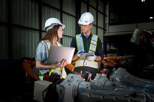 Sales manager and factory owner in suits negotiating selling robots used in the factory. Business engineers meeting and checking new machine robot. Workers walking at warehouse welding machine. photo