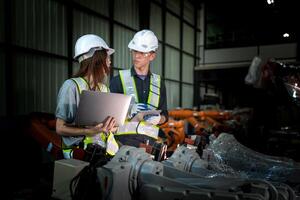 team engineers inspecting on machine with smart tablet. Worker works at heavy machine robot arm. The welding machine with a remote system in an industrial factory. Artificial intelligence concept. photo