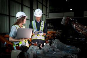 team engineers inspecting on machine with smart tablet. Worker works at heavy machine robot arm. The welding machine with a remote system in an industrial factory. Artificial intelligence concept. photo