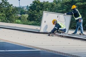 Worker Technicians are working to construct solar panels system on roof. Installing solar photovoltaic panel system. Men technicians carrying photovoltaic solar modules on roof. photo