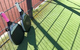 Padel racket and yellow ball behind net on a green court grass turf outdoors. Paddle is a racquet game. Professional sport concept with space for text photo