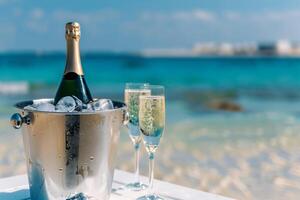 Sparkling wine in an ice bucket served on a table on a sandy beach by the blue ocean photo