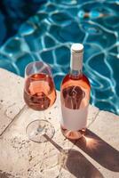 Rose wine in a bottle with white blank mock-up label and glass with blue pool in the background photo