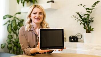 Young smiling woman showing blank tablet computer screen in office. Focus on tablet computer photo