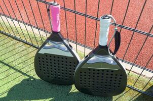Padel racket and yellow ball behind net on a green court grass turf outdoors. Paddle is a racquet game. Professional sport concept with space for text photo