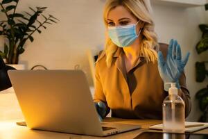 Young woman caucasian wearing gloves on hands and mask on face while working from home or at the office work by the laptop in day preventing virus spread during epidemic quarantine prevention photo