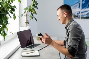 Smiling young man freelancer using laptop, studying online, working from home, happy casual guy typing on pc notebook surfing internet, enjoying distant job, sit at table. photo