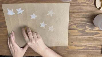 Women's hands make stamps from potatoes in form of star on craft paper. Girl decorates wrapping paper on wooden table. Gouache print. Diy and handicraft. video