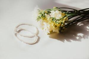 White bracelets with pearl beads on a white background with flowers. photo