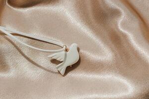 bijouterie white bird made of polymer clay on the background of silk shiny fabric photo