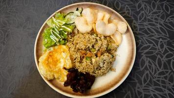 Delicious Fried Rice with Grilled Chicken and Fresh Veggie Salad on a Brown Plate with Prawn Crackers on a Patterned Tablecloth Background photo