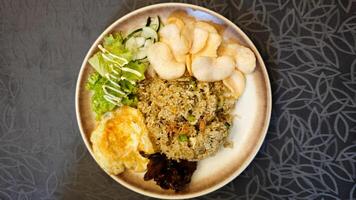 Delicious Fried Rice with Grilled Chicken and Fresh Veggie Salad on a Brown Plate with Prawn Crackers on a Patterned Tablecloth Background photo