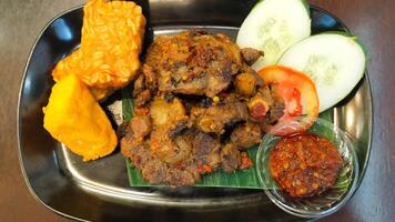 Spicy Grilled Oxtail with Tofu and Tempeh Served with Fresh Cucumber and Tomato Slices and Spicy Chili Sauce on Black Plate photo