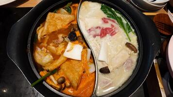 Dual Flavor Hot Pot with Spicy and Regular Broth Featuring Fresh Vegetables and Meats in a Restaurant Setting photo