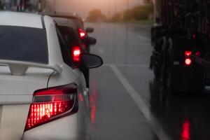 Rear side of white car with turn on brake light. on body with drop of water rain. and environment of wet from after rain storm. Cars are waiting in line at traffic lights. in Thailand. photo