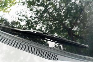 Windshield wipers placed on car windows. Reflection of trees on car windshield. Steel rod of the wiper blade has deteriorated color. photo