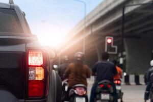 Rear side view of pickup car black color with turn signal. Motorcycle with rider stops at traffic light. Intersection under the concrete overpass. Sight of traffic in Thailand. photo