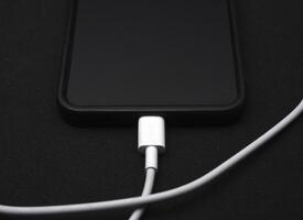 A mobile phone on a black background. A smartphone with a connection cable. photo