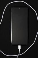 A mobile phone on a black background. A smartphone with a connection cable. photo