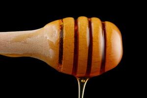 Honey dripping from a wooden dipper on a black background isolate photo