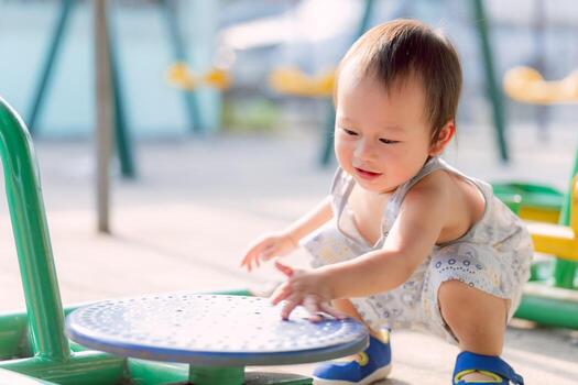 Curious Toddler on Playground. Sweet baby boy, with joyful smile, explores playground. His innocent curiosity and simple joys of childhood. Child playing with turntable of an exercise machine. photo