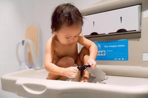 An Asian cute boy is playing with a seatbelt at the Baby Changing Station, learning to lock it. 1 year old. photo