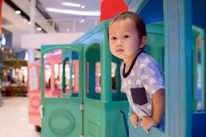 A little boy is having fun playing on the playground and in a train at the indoor, surrounded by other children and enjoying a joyful summer day. Asian Child poked his head out of a train window. photo