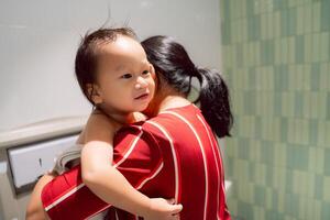 Portrait of Little boy getting dressed in family bathroom, public restroom, mother hugging toddler to wipe his diaper. Smiling child with cute expression and innocent eyes. Childcare concept. photo