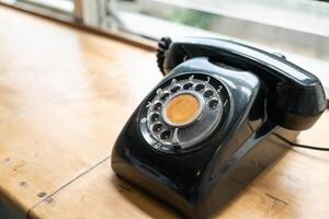 A vintage black rotary phone resting on a wooden desk. The phone has a distinct design with a circular dial containing numbered holes. copy space. photo