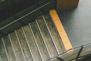 Stairs leading up to a higher level. The stairs are made of concrete and have a worn, weathered appearance. There is a yellow tactile warning strip on the side of the stairs. photo