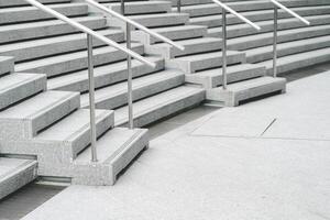 A modern staircase with wide, smooth concrete steps and sleek stainless steel handrails. The steps descend in a symmetrical pattern, creating a clean and minimalist aesthetic. photo