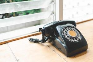 A vintage black rotary phone resting on a wooden desk. The phone has a distinct design with a circular dial containing numbered holes. copy space. photo