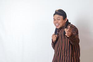 Portrait of excited Asian man in javanese cloth with blangkon hat showing product and pointing with hand and finger to the side. Sales and promotion concept. Isolated image on white background photo