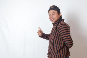 Portrait of friendly Asian man in javanese cloth with blangkon hat inviting someone to come in the most polite manner. Isolated image on white background photo