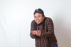 Portrait of friendly Asian man in javanese cloth with blangkon hat inviting someone to come in the most polite manner. Isolated image on white background photo