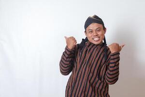 Portrait of excited Asian man in javanese cloth with blangkon hat making thumbs up hand gesture, showing approval and agreement. Isolated image on white background photo