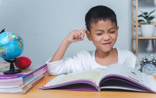The child smile thinking sitting at table with book. Education, Childhood, People, Homework and school concept. Student learning study reading book while sitting at home. photo