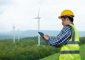 Engineer checking control electric power, Engineer man working with tablet at windmill farm Generating electricity clean energy, Wind turbine farm generator by alternative green energy. photo