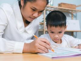 Teacher or mother helping boy writing lesson and learning to write, Education home school concept, Female tutor helping little elementary school boy with homework during individual lesson at home photo