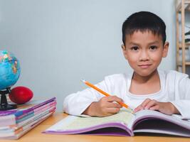 Education, Childhood, People, Homework and school concept. Student boy with book writing to notebook at home, Student learning study reading book while sitting at home. photo