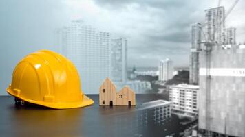 Hard hat and wooden house mockup placed at black tabletop on double exposure background of high building and construction site. Project planning presentation, project presentation and project design. photo