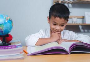 The child smile thinking sitting at table with book. Education, Childhood, People, Homework and school concept. Student learning study reading book while sitting at home. photo