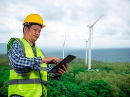 Engineer checking control electric power, Engineer man working with tablet at windmill farm Generating electricity clean energy, Wind turbine farm generator by alternative green energy. photo