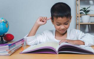 The child smile thinking sitting at table with book. Education, Childhood, People, Homework and school concept. Student learning study reading book while sitting at home. photo