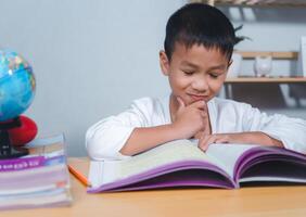 The child smile thinking sitting at table with book. Education, Childhood, People, Homework and school concept. Student learning study reading book while sitting at home. photo