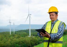 Engineer checking control electric power, Engineer man working with tablet at windmill farm Generating electricity clean energy, Wind turbine farm generator by alternative green energy. photo