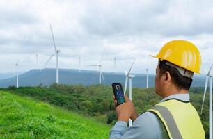 Engineer checking control electric power, Engineer man working with tablet at windmill farm Generating electricity clean energy, Wind turbine farm generator by alternative green energy. photo